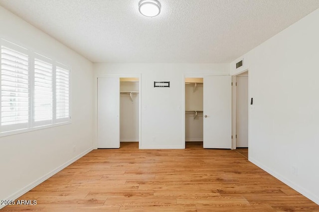 unfurnished bedroom featuring multiple closets, a textured ceiling, and light wood-type flooring