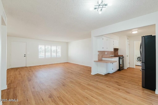 kitchen featuring stainless steel fridge, light hardwood / wood-style flooring, white cabinetry, washer / dryer, and range with two ovens