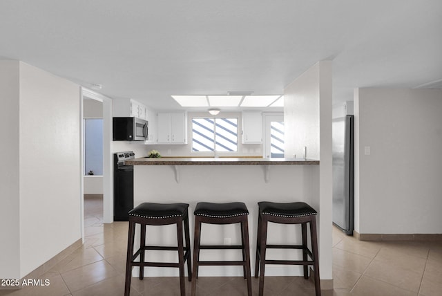 kitchen featuring light tile patterned floors, kitchen peninsula, appliances with stainless steel finishes, and white cabinetry