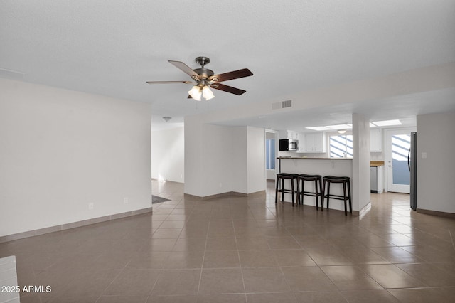 unfurnished living room with visible vents, baseboards, ceiling fan, tile patterned flooring, and a textured ceiling