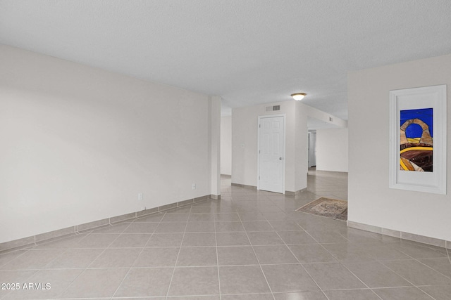 unfurnished room with a textured ceiling, tile patterned flooring, visible vents, and baseboards