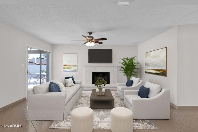 living room featuring a textured ceiling, ceiling fan, a brick fireplace, and tile patterned flooring