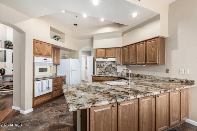 7955 E Chaparral Rd Unit 17, Scottsdale, AZ 85250 - kitchen with white appliances, arched walkways, under cabinet range hood, a peninsula, and light stone countertops
