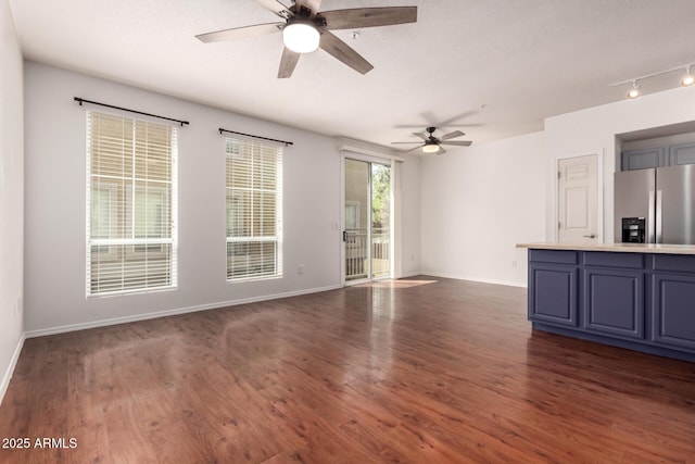 unfurnished living room with rail lighting, baseboards, a ceiling fan, and dark wood-style floors