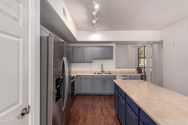 kitchen featuring stainless steel appliances, dark wood-style flooring, a sink, track lighting, and light countertops