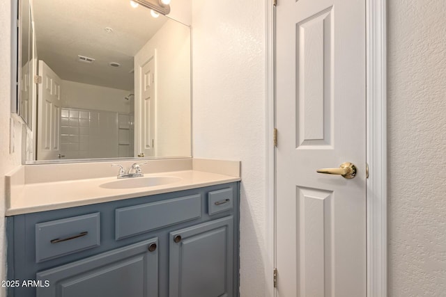 bathroom featuring vanity, a textured wall, a shower, and visible vents
