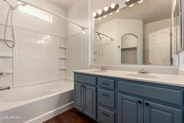bathroom featuring double vanity, washtub / shower combination, wood finished floors, and a sink