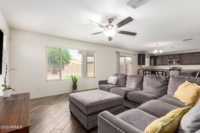 living room featuring dark wood-type flooring, ceiling fan with notable chandelier, baseboards, and visible vents