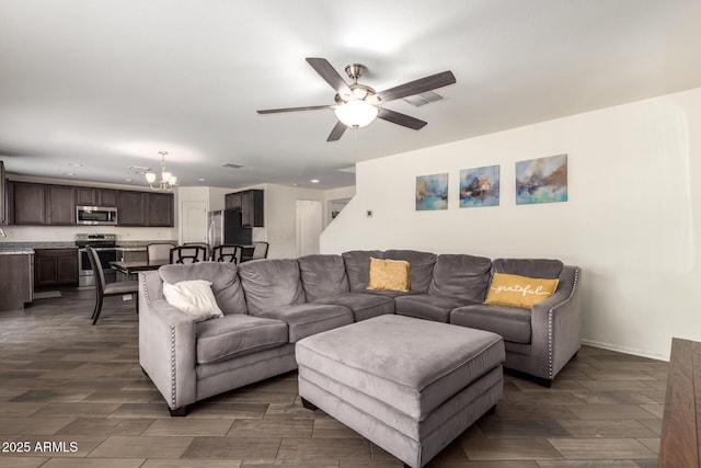living room featuring dark wood-type flooring, ceiling fan with notable chandelier, and baseboards