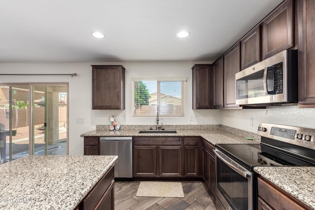 kitchen featuring light stone counters, a sink, dark brown cabinets, and stainless steel appliances