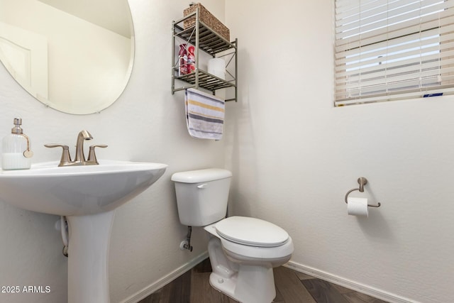 half bath featuring a sink, toilet, wood finished floors, and baseboards