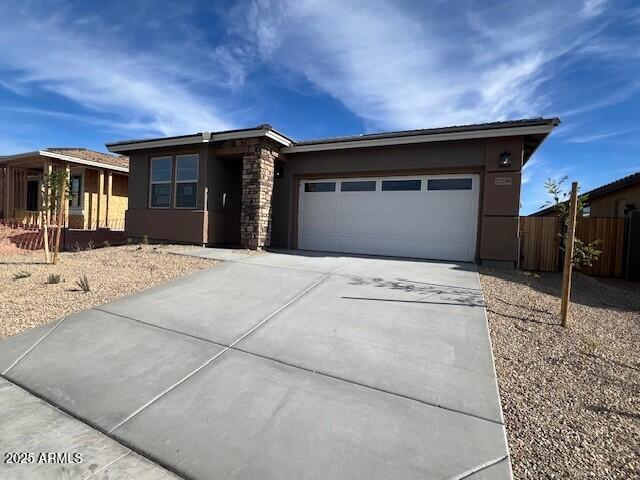 view of front of home featuring stucco siding, driveway, stone siding, fence, and a garage