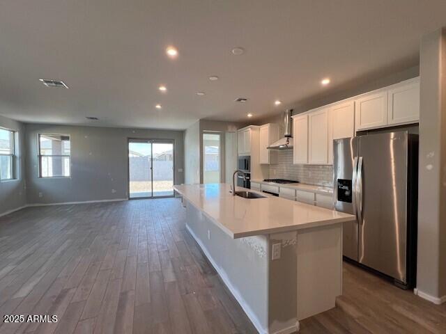 kitchen featuring white cabinetry, wall chimney range hood, stainless steel appliances, and an island with sink