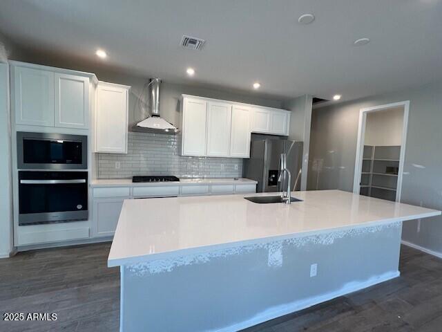 kitchen with visible vents, an island with sink, stainless steel appliances, wall chimney exhaust hood, and a sink