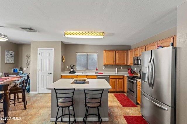kitchen with stainless steel appliances, light countertops, a sink, a kitchen island, and a breakfast bar