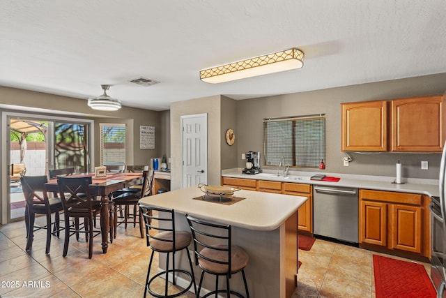 kitchen featuring dishwasher, light countertops, a sink, a center island, and a kitchen bar
