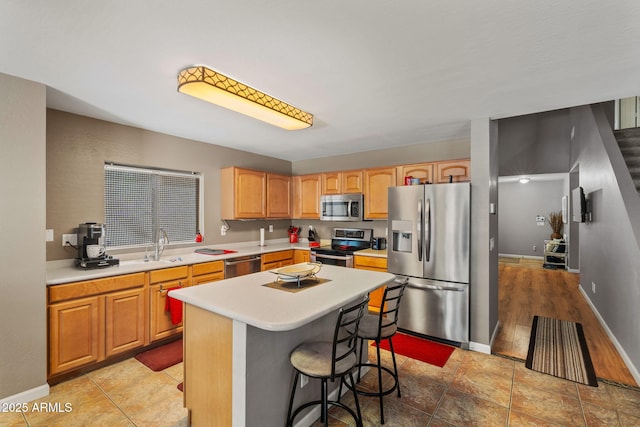 kitchen featuring appliances with stainless steel finishes, light countertops, a center island, a kitchen breakfast bar, and baseboards