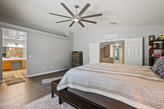 bedroom featuring lofted ceiling, wood finished floors, baseboards, ensuite bath, and ceiling fan