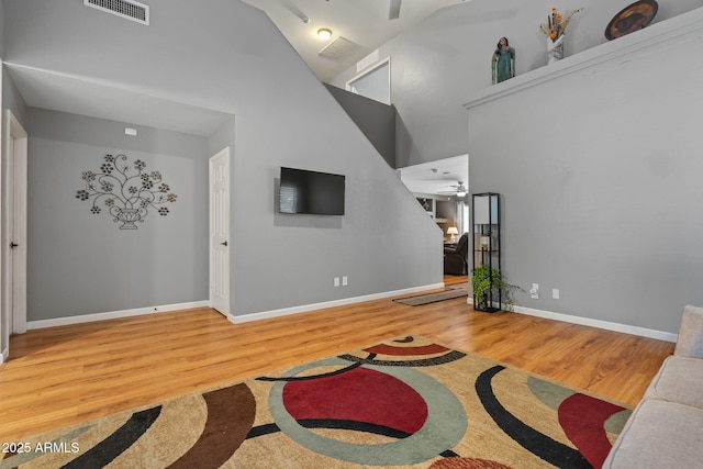 living area featuring a high ceiling, wood finished floors, baseboards, and ceiling fan
