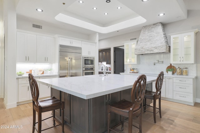 kitchen with a spacious island, a kitchen bar, built in appliances, a raised ceiling, and white cabinets