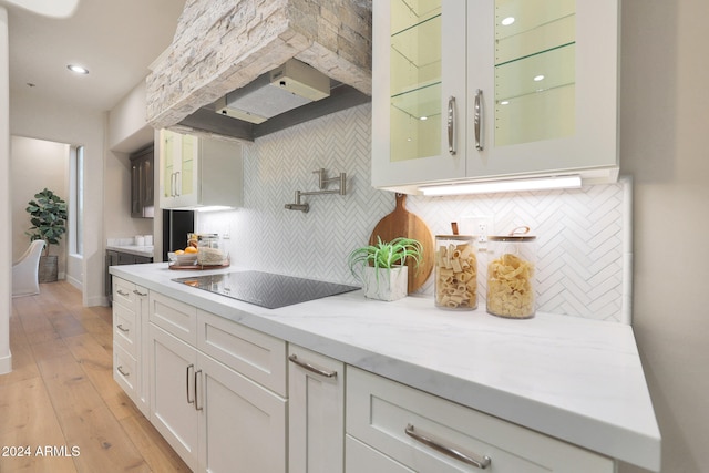 kitchen with white cabinets, backsplash, black electric stovetop, light hardwood / wood-style floors, and light stone countertops