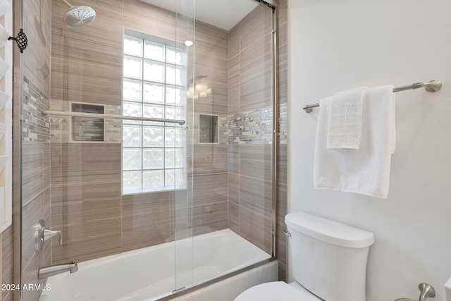 bathroom with a wealth of natural light, shower / bath combination with glass door, and toilet