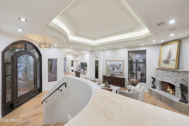 interior space with a stone fireplace, wood-type flooring, a tub, vanity, and a tray ceiling