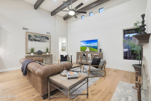 living room with ceiling fan, beam ceiling, light wood-type flooring, and a high ceiling