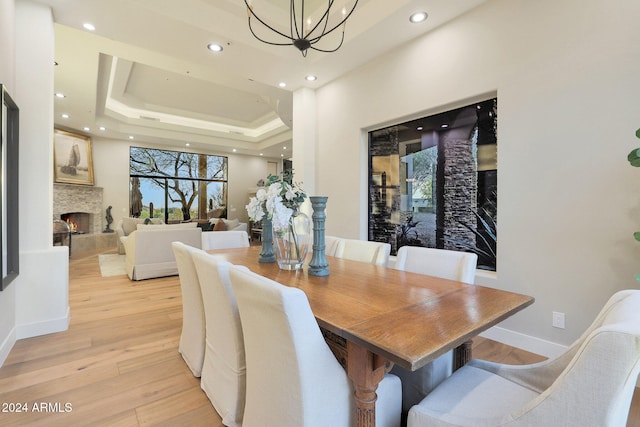 dining area featuring an inviting chandelier, a fireplace, a raised ceiling, and light wood-type flooring