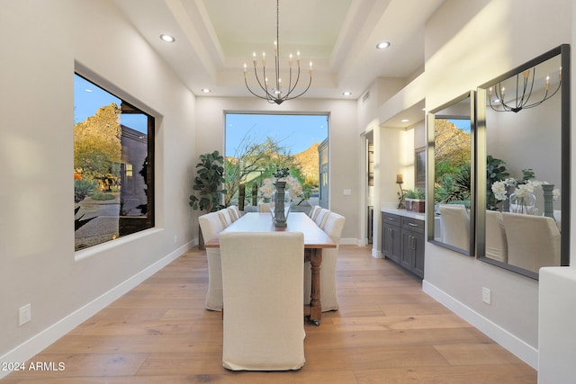 dining area featuring plenty of natural light, an inviting chandelier, light wood-type flooring, and a tray ceiling