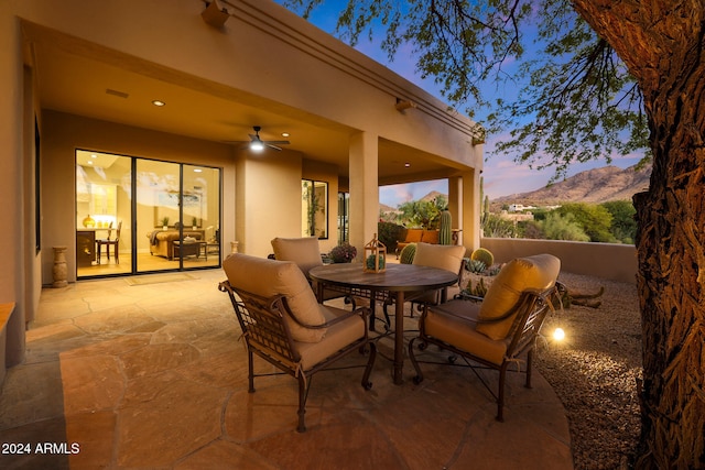 patio terrace at dusk featuring a mountain view and ceiling fan