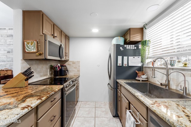 kitchen with light tile patterned flooring, stainless steel appliances, light stone countertops, and sink