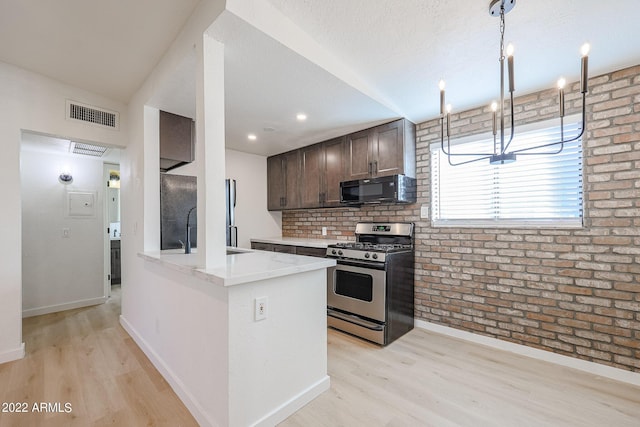 kitchen featuring stainless steel gas range oven, visible vents, brick wall, black microwave, and dark brown cabinetry