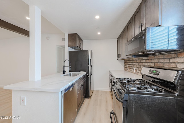 kitchen with tasteful backsplash, light stone countertops, light wood-style floors, stainless steel appliances, and a sink