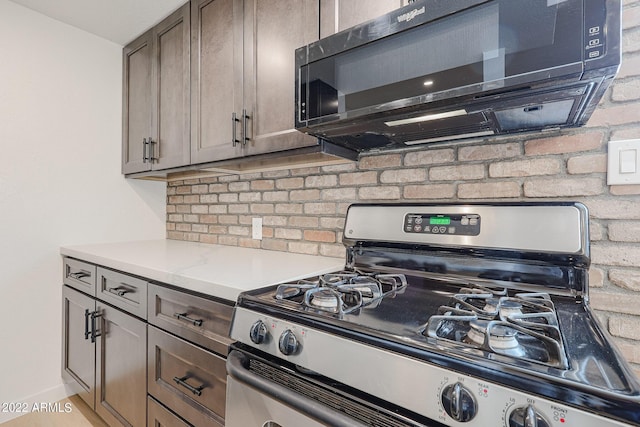 kitchen with gas stove, backsplash, black microwave, and light countertops