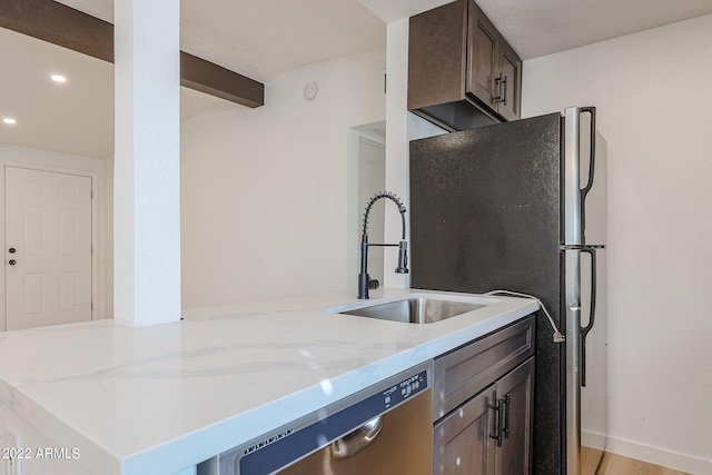 kitchen featuring a sink, stainless steel appliances, baseboards, dark brown cabinetry, and light stone countertops