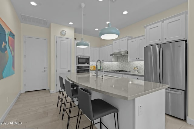 kitchen with pendant lighting, sink, appliances with stainless steel finishes, white cabinets, and a center island with sink