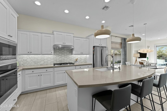 kitchen with pendant lighting, white cabinetry, appliances with stainless steel finishes, and a center island with sink