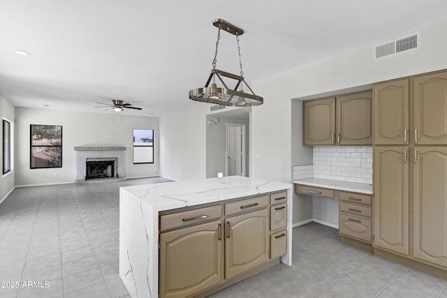 kitchen with pendant lighting, ceiling fan, tasteful backsplash, light stone counters, and built in desk