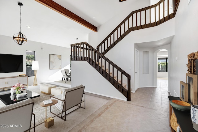 tiled living room with a wealth of natural light, beamed ceiling, and an inviting chandelier