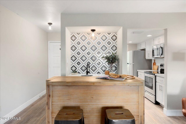 kitchen featuring appliances with stainless steel finishes, sink, light hardwood / wood-style floors, white cabinetry, and a breakfast bar area