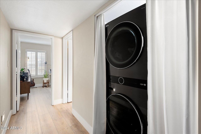 laundry area featuring stacked washing maching and dryer, a textured ceiling, and light wood-type flooring