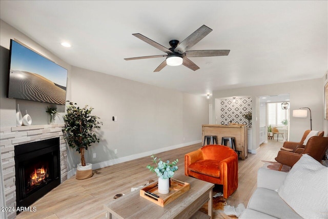 living room with ceiling fan, a stone fireplace, and light hardwood / wood-style flooring