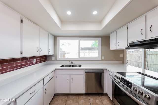 kitchen featuring appliances with stainless steel finishes, a tray ceiling, sink, white cabinets, and light tile patterned flooring