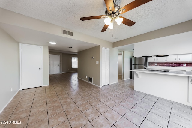 kitchen with a textured ceiling, stainless steel fridge, light tile patterned floors, decorative backsplash, and ceiling fan