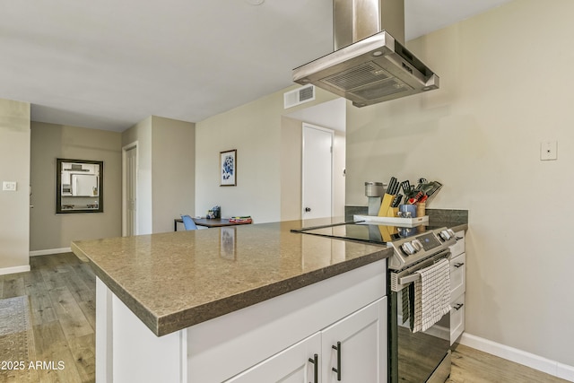 kitchen with white cabinets, electric range, island range hood, and light hardwood / wood-style floors