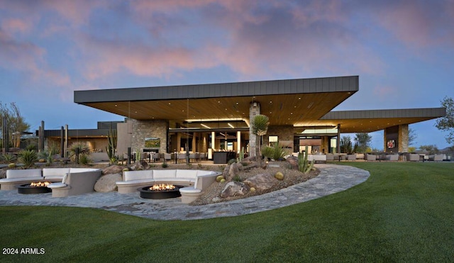 back house at dusk with a lawn and an outdoor living space with a fire pit