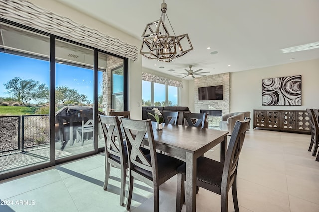 tiled dining space with a fireplace and ceiling fan with notable chandelier