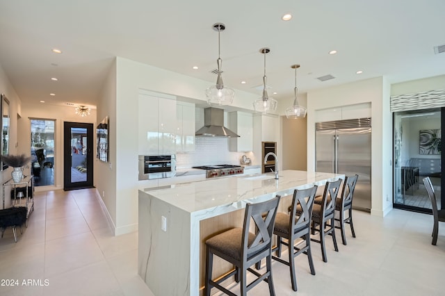 kitchen featuring a breakfast bar, wall chimney exhaust hood, appliances with stainless steel finishes, a large island, and white cabinetry