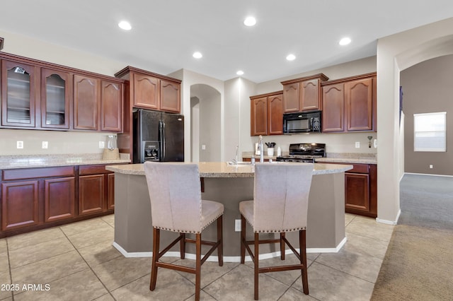 742 E Kingbird Dr, Gilbert, AZ 85297 - kitchen with black appliances, arched walkways, an island with sink, a kitchen bar, and light tile patterned flooring